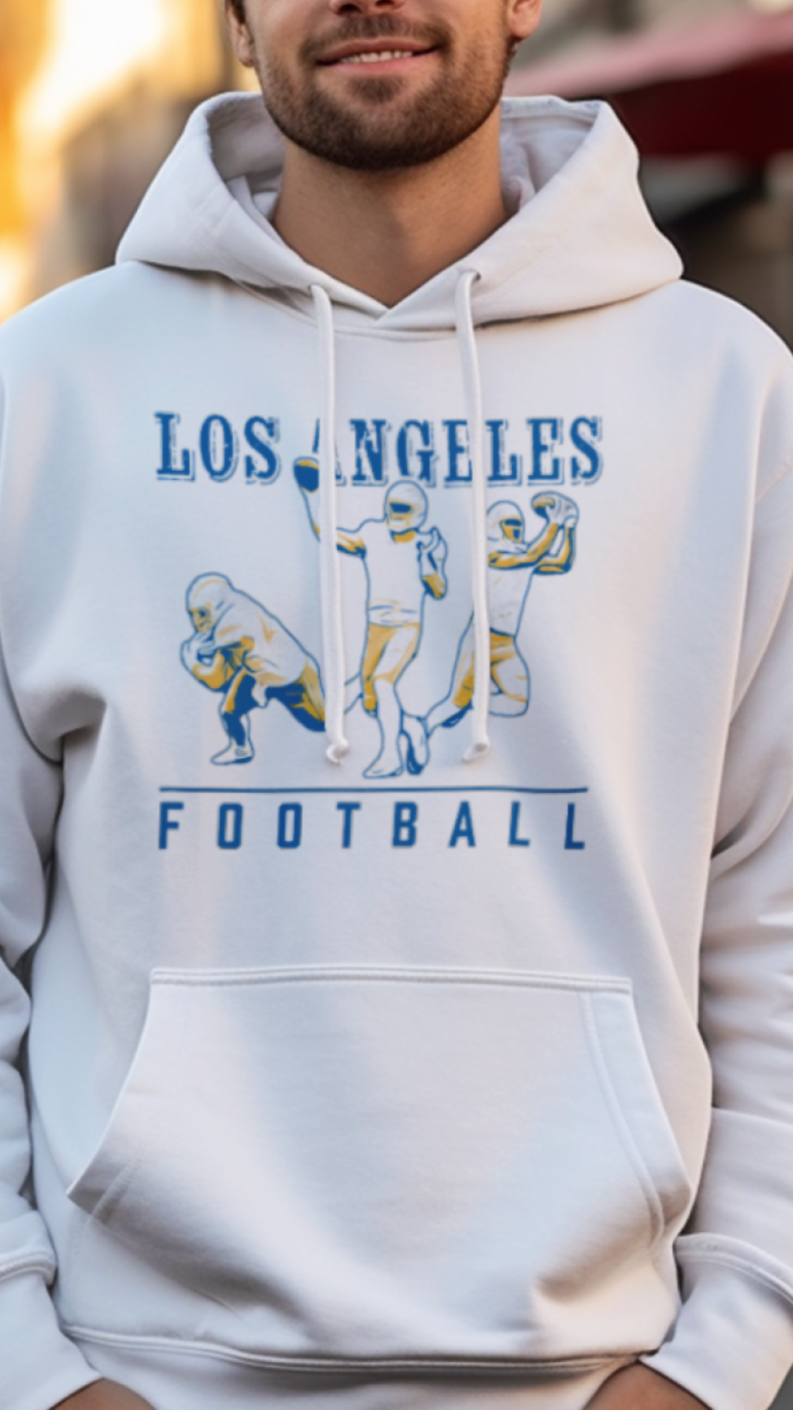 Person wearing a white hoodie with 'Los Angeles Football' design on a street.