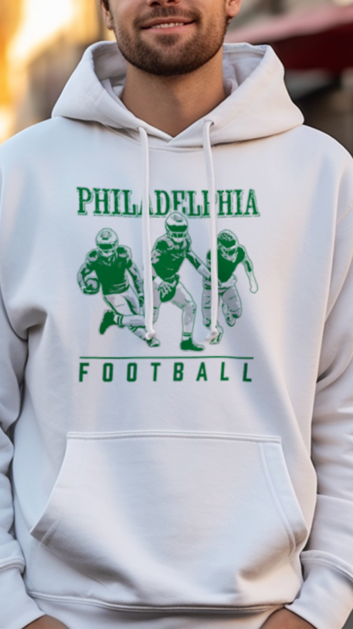 Person wearing a white hoodie with 'Philadelphia Football' design on a street.