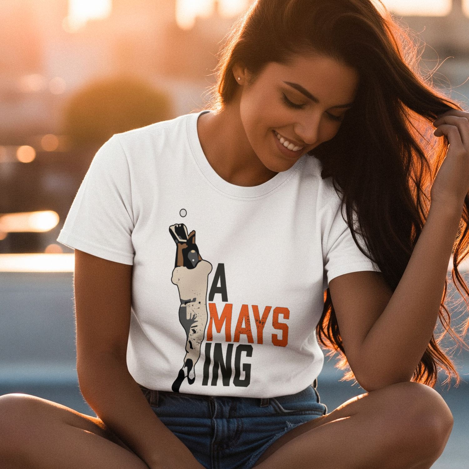 Woman wearing a white t-shirt with a graphic design sitting by a waterfront at sunset.