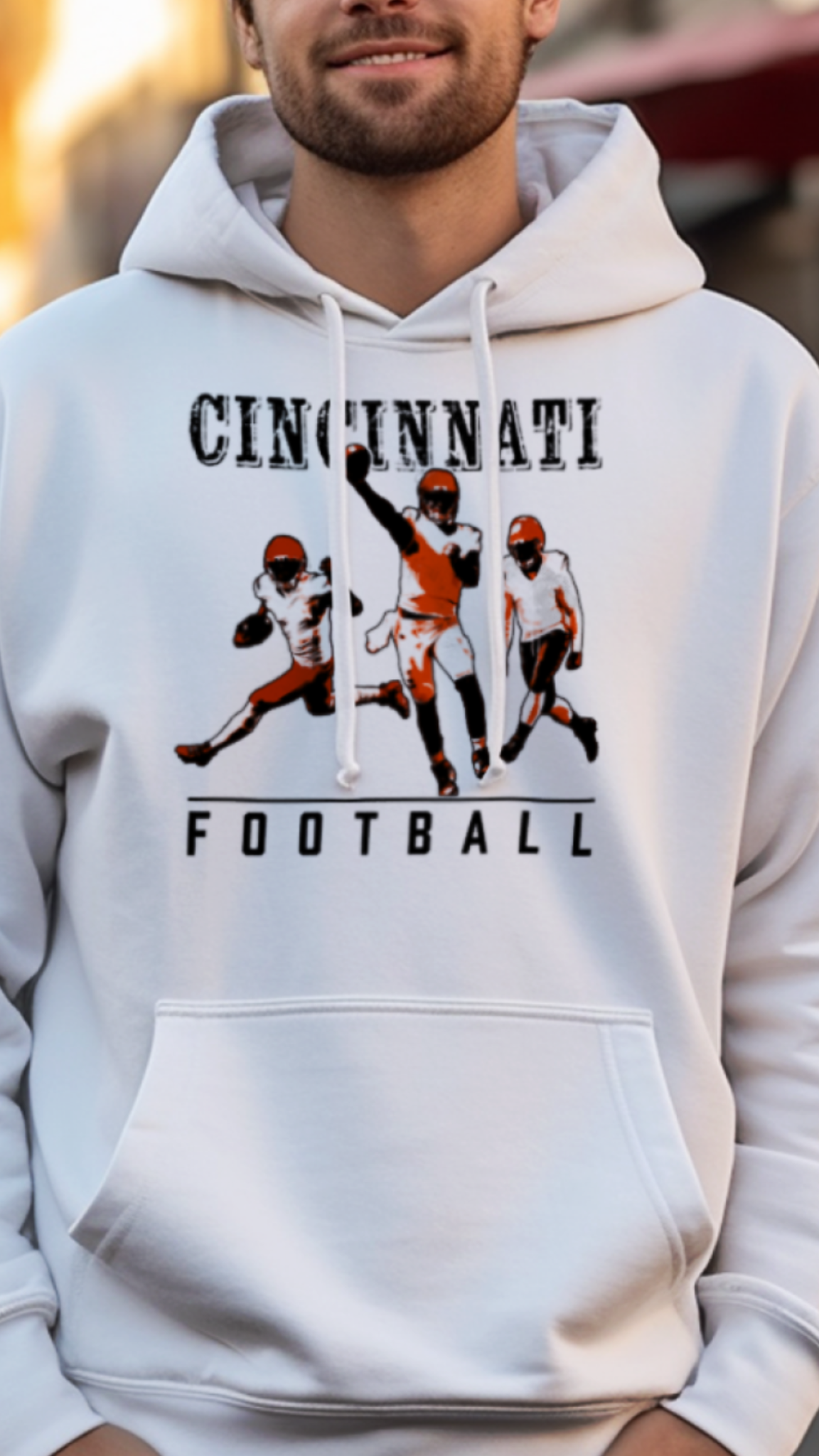 Man wearing a white hoodie with 'Cincinnati Football' design on a street.