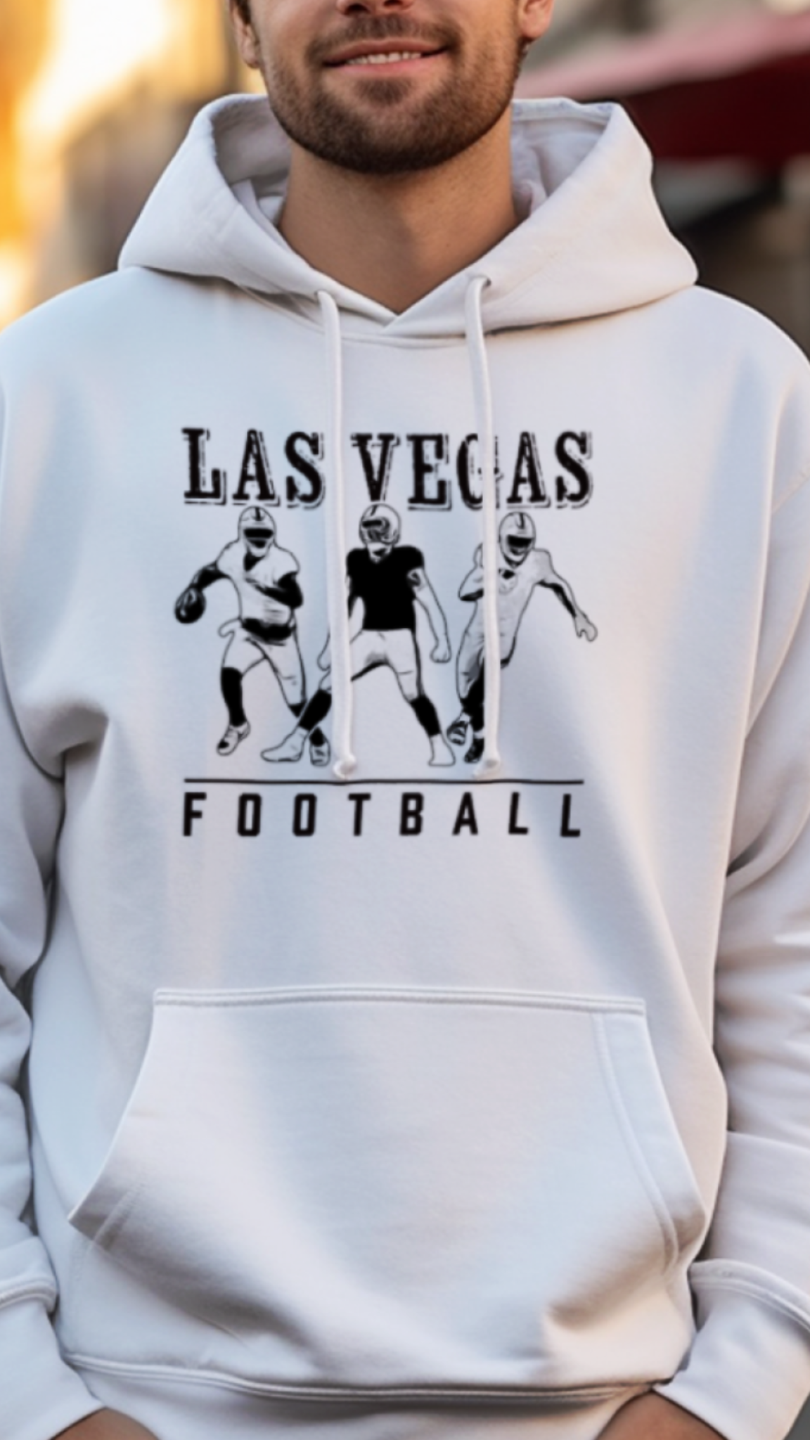 Man wearing a white hoodie with 'Las Vegas Football' text and graphics on a street background