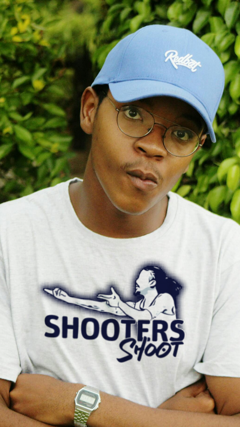 Person wearing a white t-shirt with a graphic and text, standing against a green leafy background
