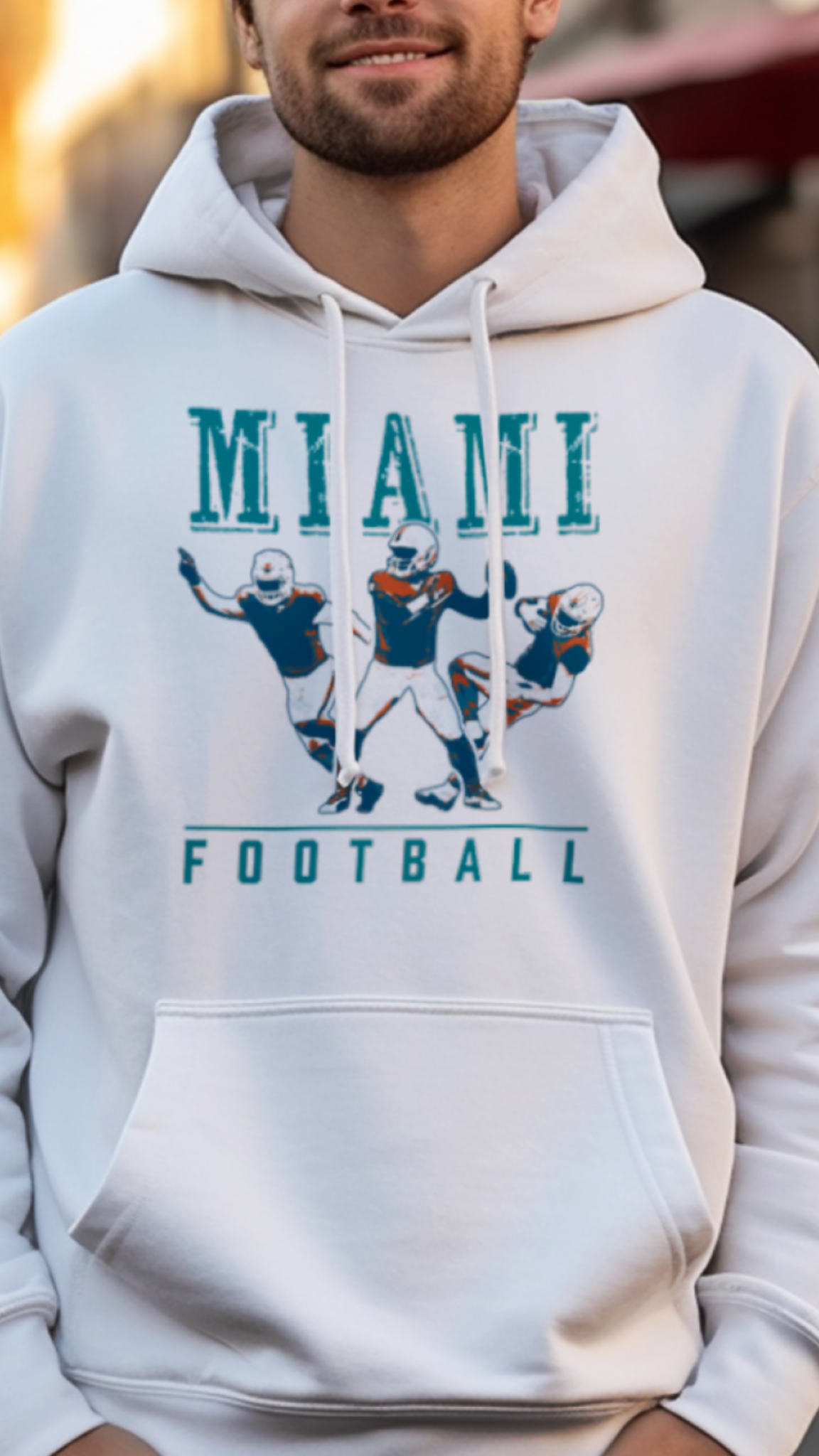 Man wearing a white hoodie with 'Miami Football' design on a street.