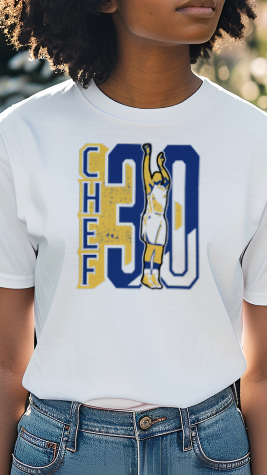 Person wearing a white t-shirt with colorful design, standing outdoors with greenery in the background