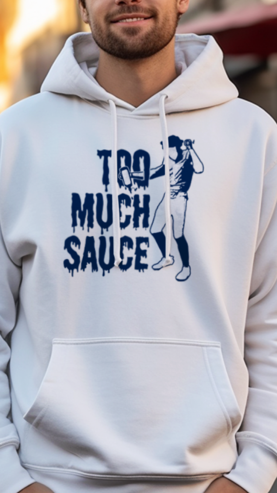 Man wearing a white hoodie with 'Too Much Sauce' text and graphic, standing on a street.