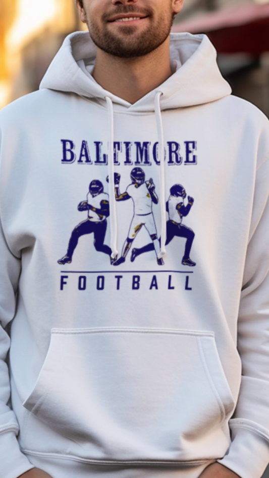 Man wearing a white hoodie with 'Baltimore Football' design on a city street.